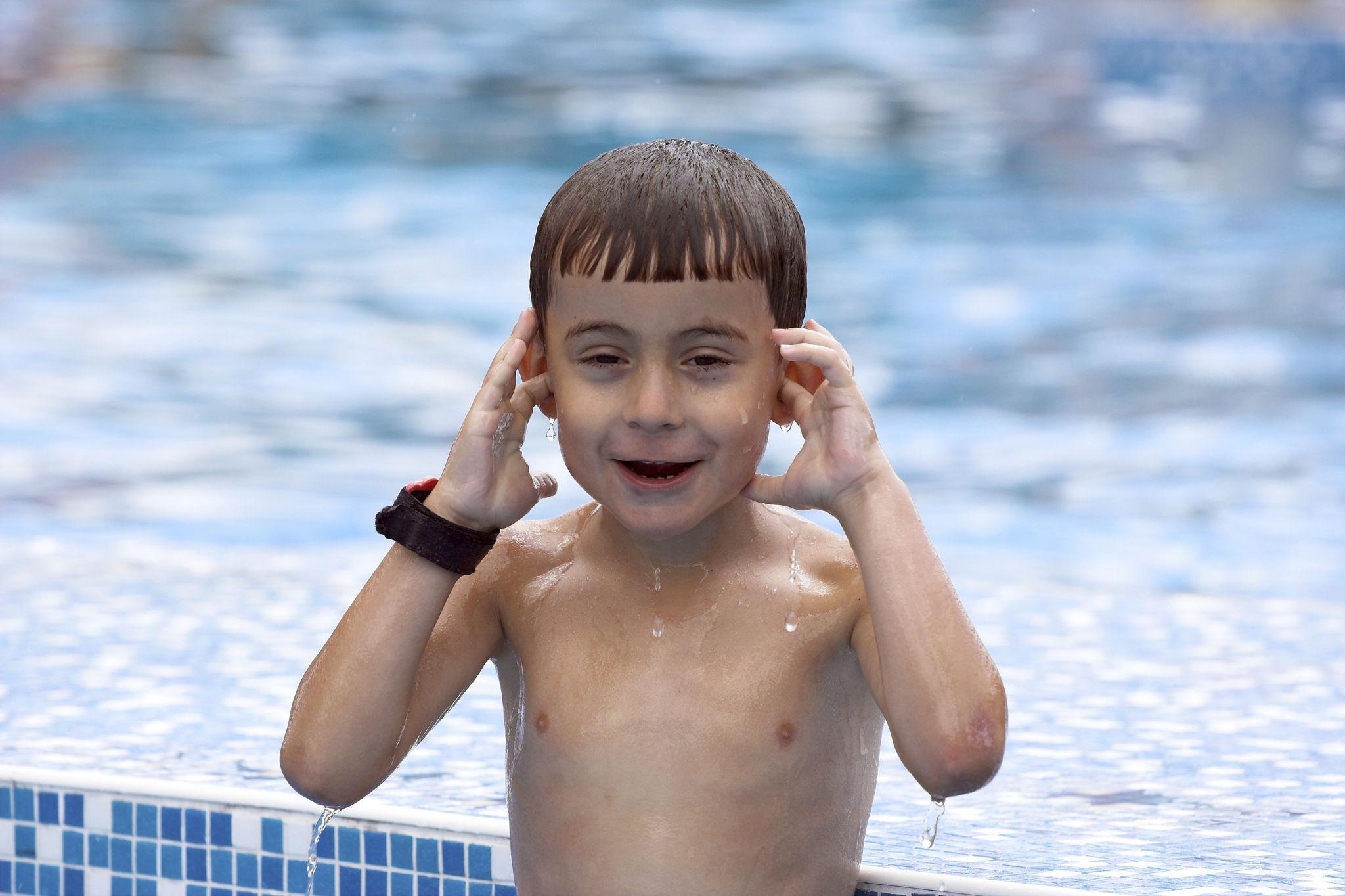 Young boy at a swimming pool gently holding his ear after swimming.