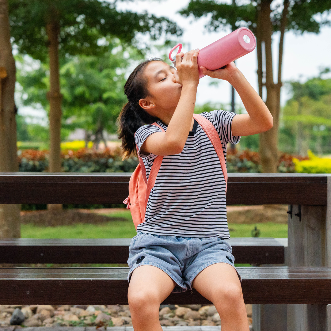 Young girl drinking water outdoors to stay hydrated on a warm summer day."